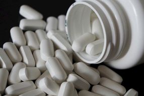 An open bottle of white pill capsules spilling out.