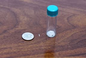A vial next to a dime (for scale) of non-opioid micropellet implants for chronic pain.